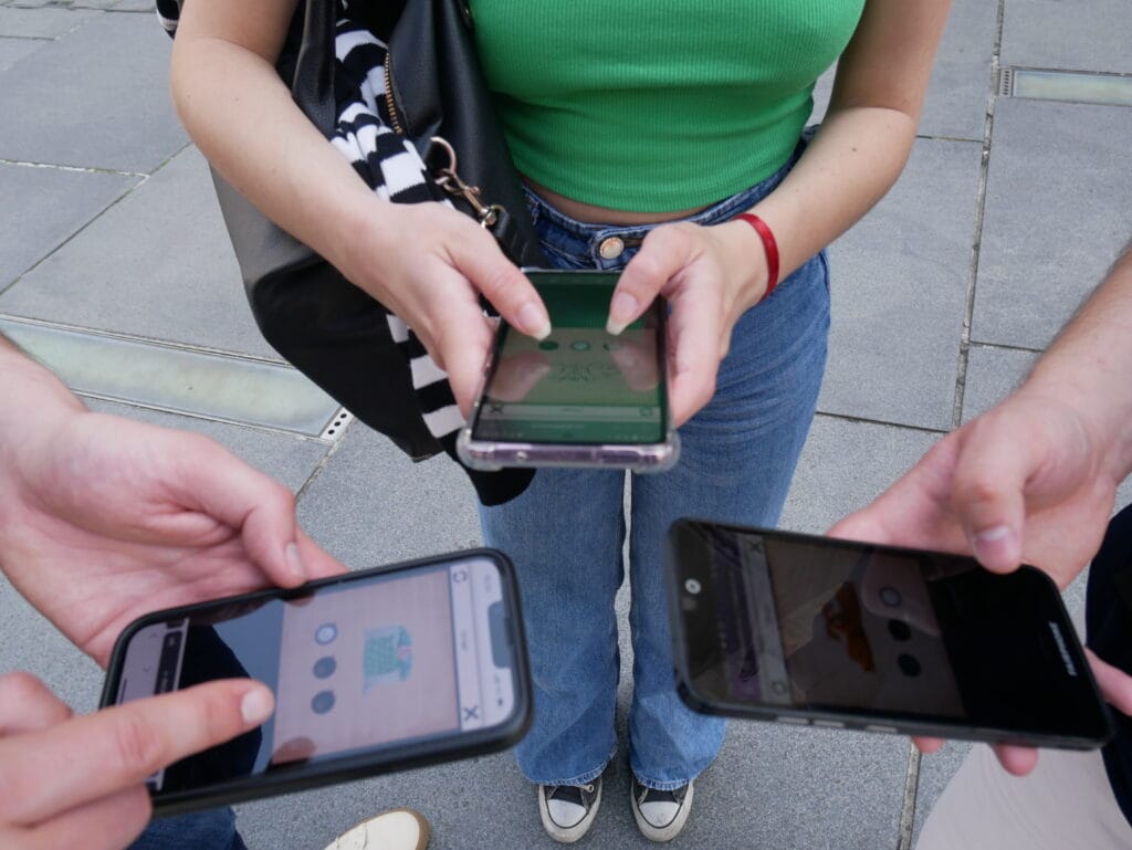 Trois joueurs regardent leur téléphone pour répondre à une énigme digitale. Gros plan sur les téléphones. 