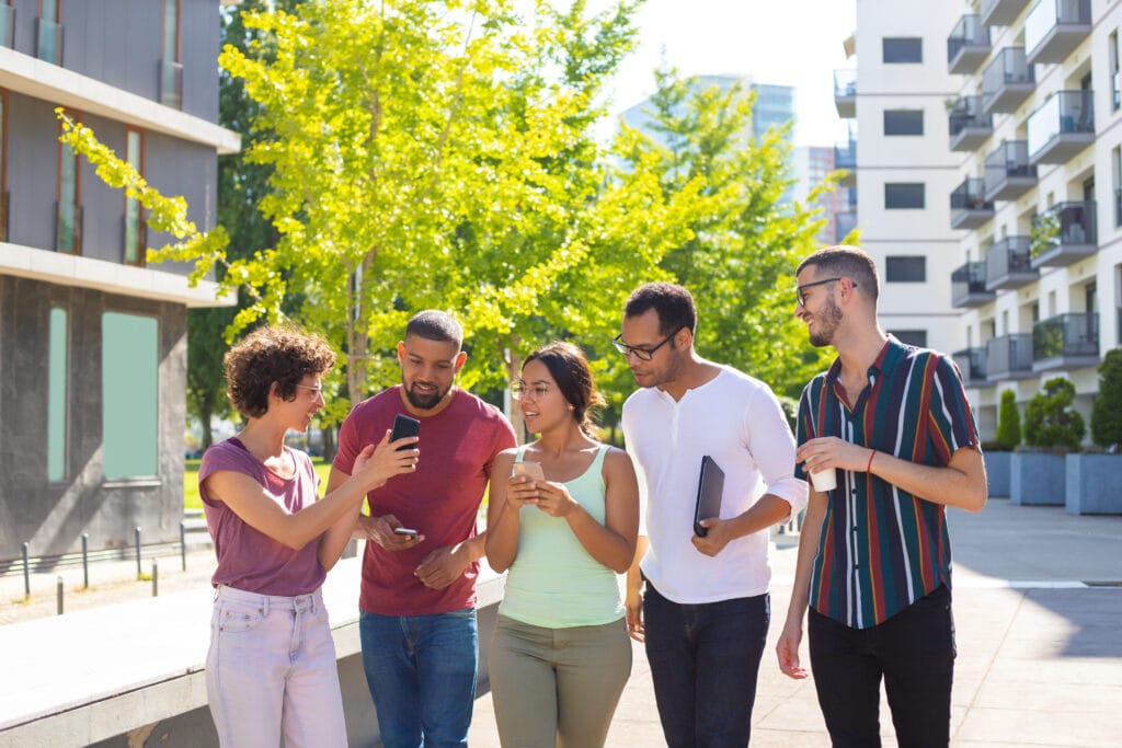 Groupe de 5 collaborateurs essayant de déchiffrer une énigme sur un téléphone, en extérieur. Représentation d'un team building. 
